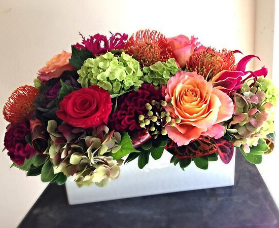 A floral arrangement of multi-colored Get Well Flowers, including roses and hydrangeas, in a white rectangular vase.